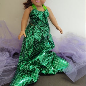 Puede incluir: Un disfraz de sirena verde para una mu&ntilde;eca. El disfraz presenta un top y una cola de color verde iridiscente con estampado de escamas. La cola es larga y fluida, con una aleta puntiaguda en el extremo.