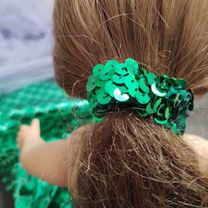Puede incluir: Coleta de pelo de lentejuelas verdes para una mu&ntilde;eca. La coleta est&aacute; hecha de peque&ntilde;as lentejuelas redondas que est&aacute;n cosidas juntas en un c&iacute;rculo.