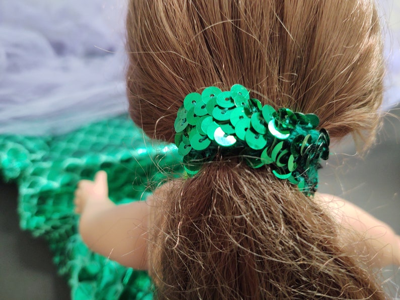 Puede incluir: Coleta de pelo de lentejuelas verdes para una mu&ntilde;eca. La coleta est&aacute; hecha de peque&ntilde;as lentejuelas redondas que est&aacute;n cosidas juntas en un c&iacute;rculo.