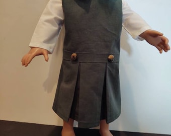 May include: A green pinafore dress with a white collared shirt underneath. The dress has a pleated skirt and two gold buttons on the front.