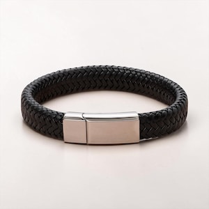 May include: A black braided leather bracelet featuring a polished silver-tone metal rectangular clasp. The bracelet has a thick, woven texture and a smooth, metallic closure that secures the two ends of the leather band together in a loop.