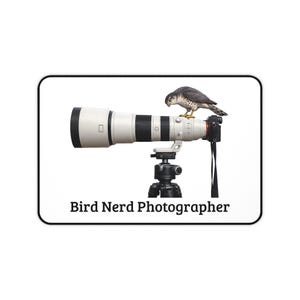 May include: A white and black telephoto lens mounted on a tripod, with a small bird perched on top. The text "Bird Nerd Photographer" is displayed below the equipment.