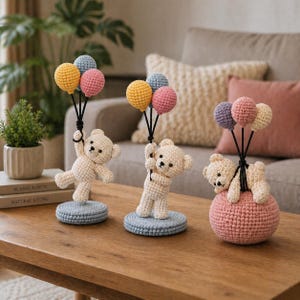 Puede incluir: Tres figuras de osos de peluche de ganchillo. Cada oso sostiene un grupo de globos de colores. Un oso está de pie sobre una base azul, otro sobre una esfera rosa y el tercero sobre una base azul. Los globos son amarillos, rosas y azules.