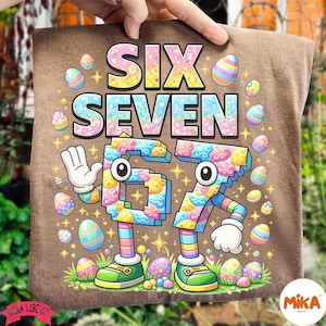 May include: Brown t-shirt with the words "SIX SEVEN" in colorful letters. The numbers 6 and 7 are designed as cartoon characters with arms, legs, and shoes. Easter eggs and stars surround the text and numbers.