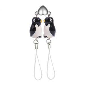 May include: A pair of penguin-shaped charms, each with black and white bodies and yellow beaks, connected by a silver heart-shaped element. White cords hang from the bottom of each penguin. The charms are likely intended for use as phone accessories or keychains.