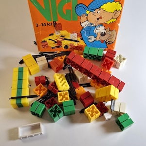 Könnte beinhalten: Vintage "NICI" Bausteine-Set in einer orangefarbenen Box. Die Box zeigt eine Cartoon-Illustration eines Jungen und eines Hundes. Das Set enthält verschiedene farbige Blöcke in Rot, Gelb, Grün und Weiß.