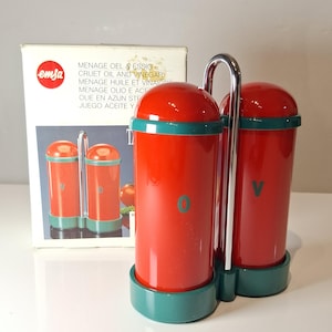 Peut inclure: Un ensemble de cruets à huile et vinaigre vintage, rouge et turquoise, avec une poignée chromée. L'ensemble comprend deux récipients cylindriques avec des couvercles rouges et des bases turquoise, marqués "O" et "V". La boîte d'origine, avec la marque "emsa", est visible.
