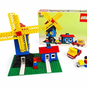 Op de afbeelding: Een vintage LEGO set 362 met een blauwe windmolen met gele wieken, een klein blauw huisje met een rood dak, een rode vrachtwagen en twee minifiguren op een groene grondplaat. De originele doos toont de windmolen, het huisje en de vrachtwagen.