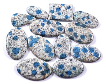 May include: A collection of polished K2 stone cabochons in various shapes, including ovals and a rectangle. The stones feature a speckled white and gray base with vibrant blue orb-like patterns. These gemstones are ideal for jewelry making.