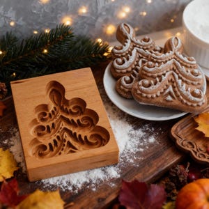 May include: A wooden Christmas tree-shaped cookie mold sits next to a plate of decorated cookies dusted with powdered sugar. The cookies have intricate designs. Flour is sprinkled on the wooden surface, and the background includes a sprig of pine and fairy lights.