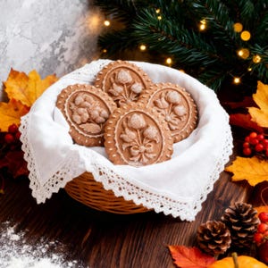 May include: A wicker basket filled with four intricately decorated gingerbread cookies. Each cookie features a floral design with white icing details. The basket sits on a wooden surface, surrounded by autumn leaves and pine cones, creating a festive, seasonal display.