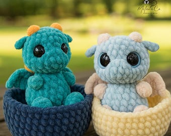 May include: Two handmade crochet dragon plushies. One is teal with orange accents, the other is light blue with tan accents. Each dragon sits in a matching crochet basket. The dragons have large black eyes. The background is blurred.