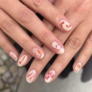 May include: Oval-shaped nails with a light beige polish, decorated with red line art of seafood and dining items. Designs include prawns, a crab, a fish, a wine glass, a bottle, a knife, and a spoon.