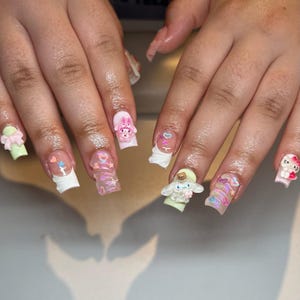 Peut inclure: Ongles en acrylique longs et carr&eacute;s avec divers motifs en 3D. Les ongles pr&eacute;sentent des couleurs pastel, notamment du rose, du vert et du blanc, et sont orn&eacute;s de personnages de dessins anim&eacute;s, de n&oelig;uds et de c&oelig;urs.