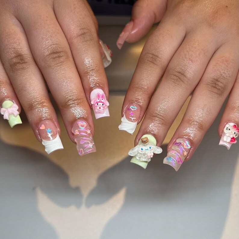 Peut inclure: Ongles en acrylique longs et carr&eacute;s avec divers motifs en 3D. Les ongles pr&eacute;sentent des couleurs pastel, notamment du rose, du vert et du blanc, et sont orn&eacute;s de personnages de dessins anim&eacute;s, de n&oelig;uds et de c&oelig;urs.