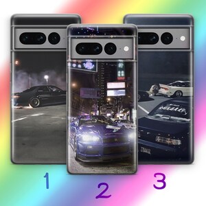 Puede incluir: Tres fundas para teléfono con diseños de coches. Las fundas presentan imágenes de coches por la noche, una de ellas con un coche azul con faros brillantes. Las otras dos fundas muestran coches negros en una calle.
