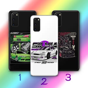 Op de afbeelding: Drie smartphonehoesjes met autografische ontwerpen. Het linkerhoesje is zwart met groene auto-illustraties en LZMFG-tekst. Het middelste hoesje is wit met een witte Silvia-auto, een paarse cirkel en tekst. Het rechterhoesje is zwart met tekst.