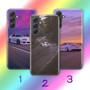 Puede incluir: Tres fundas de teléfono con diseños de coches. La primera funda presenta un coche deportivo blanco en una carretera con un fondo de puesta de sol. La segunda funda muestra un coche blanco en una carretera sinuosa. La tercera funda muestra un coche deportivo blanco con un fondo de puesta de sol.