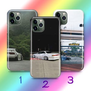 May include: Three smartphone cases featuring automotive photography. The first shows a white car on a road near trees. The second displays a white sedan parked on concrete at night. The third depicts a car drifting on a road under a highway overpass.