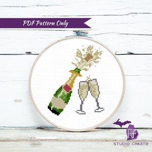 Könnte beinhalten: Ein Kreuzstichmuster einer Champagnerflasche, die mit zwei Champagnergläsern knallt. Die Flasche ist grün und gold, die Gläser sind klar und die Blasen sind weiß.