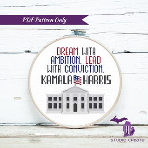 May include: A cross-stitch pattern featuring a white house with the text "DREAM WITH AMBITION. LEAD WITH CONVICTION. KAMALA HARRIS" in red, white, and blue.