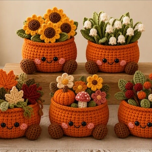May include: Five crocheted orange pots with smiling faces, each containing different plants. The pots feature small brown feet and pink cheeks. The plants include sunflowers, lily of the valley, autumn leaves, a pumpkin, a mushroom, and berries.