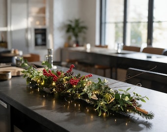 May include: A long, horizontal festive centrepiece featuring evergreen branches, bright red berries, pinecones, and dried citrus slices. The arrangement is intertwined with thin, warm-toned string lights, creating a glowing effect across the foliage.