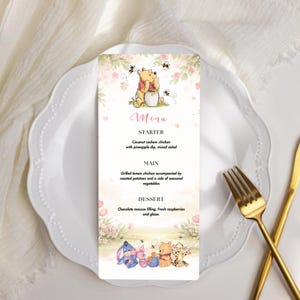 May include: A menu card featuring Winnie the Pooh characters. The menu card has a floral design with the word "Menu" at the top. The menu includes a starter, main course, and dessert. The card is on a white plate with gold silverware.