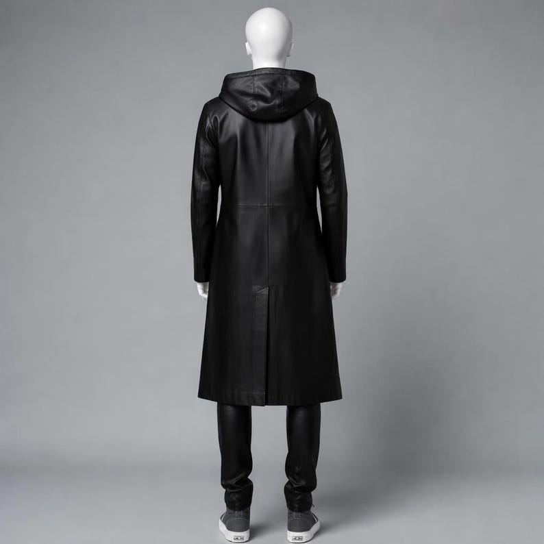 Puede incluir: Un abrigo largo de cuero negro con capucha, exhibido en un maniqu&iacute;. El abrigo llega hasta los tobillos y tiene un corte entallado. El maniqu&iacute; tambi&eacute;n lleva pantalones negros y zapatillas grises.