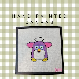 May include: Hand-painted canvas featuring a pixelated Furby design. The artwork showcases a purple Furby with pink ears, blue eyes, and yellow feet, set against a white background. The words "HAND PAINTED CANVAS" are displayed above the image.