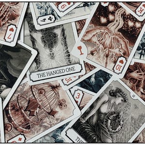 Op de afbeelding: Een verzameling tarotkaarten met gedetailleerde illustraties in sepiatinten. De kaarten tonen verschillende kleuren, getallen en titels zoals "The Hanged One". De kunstwerken omvatten figuren, symbolen en sc&egrave;nes, met rode kleursymbolen.