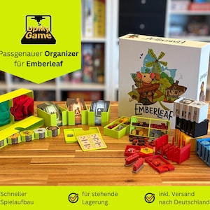 Può includere: Un set di organizzatori di giochi da tavolo per Emberleaf, con vari contenitori gialli, rossi, blu e verdi. La scatola del gioco Emberleaf è visibile, con un'illustrazione stravagante di un topo e un mulino a vento. Il testo "UpMy Game" è visibile.