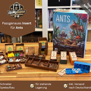 Könnte beinhalten: Ein braunes Insert für das Brettspiel "Ants" mit verschiedenen Fächern für Spielsteine. Die Spielbox ist im Hintergrund zu sehen, zusammen mit verschiedenen Spielkomponenten. Das Insert dient dazu, den Inhalt des Spiels zu organisieren und aufzubewahren.