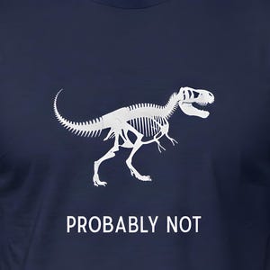 May include: Navy blue t-shirt featuring a white Tyrannosaurus Rex skeleton graphic. Below the graphic, the text reads "PROBABLY NOT". The shirt is made of a soft material.