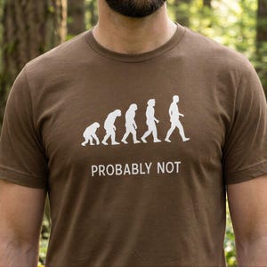 May include: Brown t-shirt featuring a white evolution graphic and the text "PROBABLY NOT". The graphic depicts the evolution of man, with the final figure walking upright. The shirt is made of a soft material.