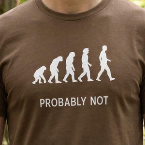 May include: Brown t-shirt with a white evolution graphic and the text "PROBABLY NOT". The graphic depicts the evolution of man, with the final figure walking upright.