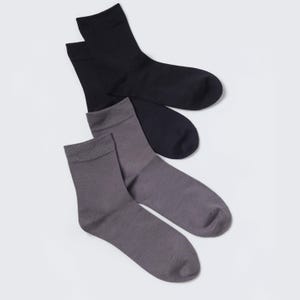 May include: A pair of solid black crew socks and a pair of solid grey crew socks. The socks feature a ribbed cuff at the top and a smooth knit texture throughout the foot and ankle area. The black socks are positioned above the grey socks.