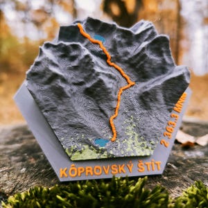 Può includere: Una mappa topografica 3D grigia e arancione di Kôprovský štít, con un sentiero arancione e laghi blu. Il testo "Kôprovský štít" è arancione. L'altitudine della vetta è di 2.363,3 metri.