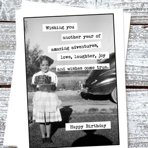 Puede incluir: Una foto en blanco y negro de una ni&ntilde;a sosteniendo un pastel que dice "Merry". El texto en la tarjeta dice "Wishing you another year of amazing adventures, love, laughter, joy and wishes come true. Happy Birthday."