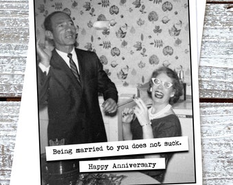 Puede incluir: Una foto en blanco y negro de una pareja en una cocina. El hombre sostiene un vaso con algo y la mujer sonríe y sostiene un cigarrillo. El texto en la tarjeta dice "Estar casado contigo no es malo. Feliz aniversario."