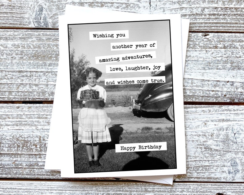 Puede incluir: Una foto en blanco y negro de una ni&ntilde;a sosteniendo un pastel que dice "Merry". El texto en la tarjeta dice "Wishing you another year of amazing adventures, love, laughter, joy and wishes come true. Happy Birthday."