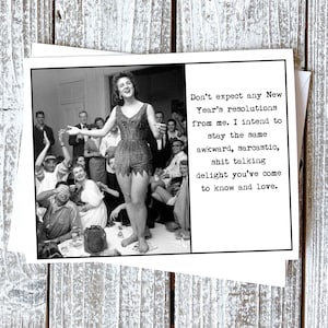 May include: Black and white greeting card featuring a vintage photograph of a woman in a costume, surrounded by people. The card includes text that reads, "Don't expect any New Year's resolutions from me. I intend to stay the same awkward, sarcastic, shit talking delight you've come to know and love."