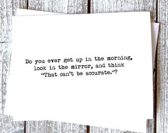 May include: White greeting card with the text: "Do you ever get up in the morning, look in the mirror, and think 'That can't be accurate.'?" The card is on a wooden surface.