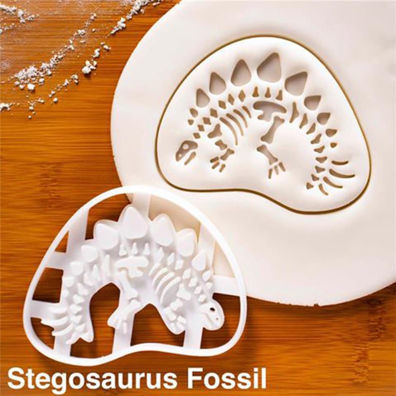 May include: A white plastic stegosaurus fossil cookie cutter next to a white imprint of the same design on a white surface. The text "Stegosaurus Fossil" is at the bottom of the image.