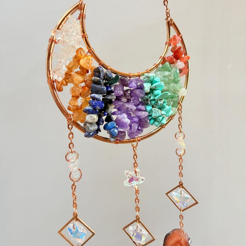 Pu&ograve; includere: Un ornamento da parete a forma di mezzaluna color rame. La luna &egrave; riempita di pietre preziose colorate disposte a forma di arcobaleno. Cristalli trasparenti, ciondoli a forma di stella e cristalli quadrati pendono dal basso.