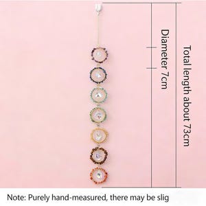 May include: A hanging chakra suncatcher featuring seven rings with gemstones and crystals. Total length is about 73cm, diameter 7cm. The rings are in various colours. The suncatcher hangs from a chain.