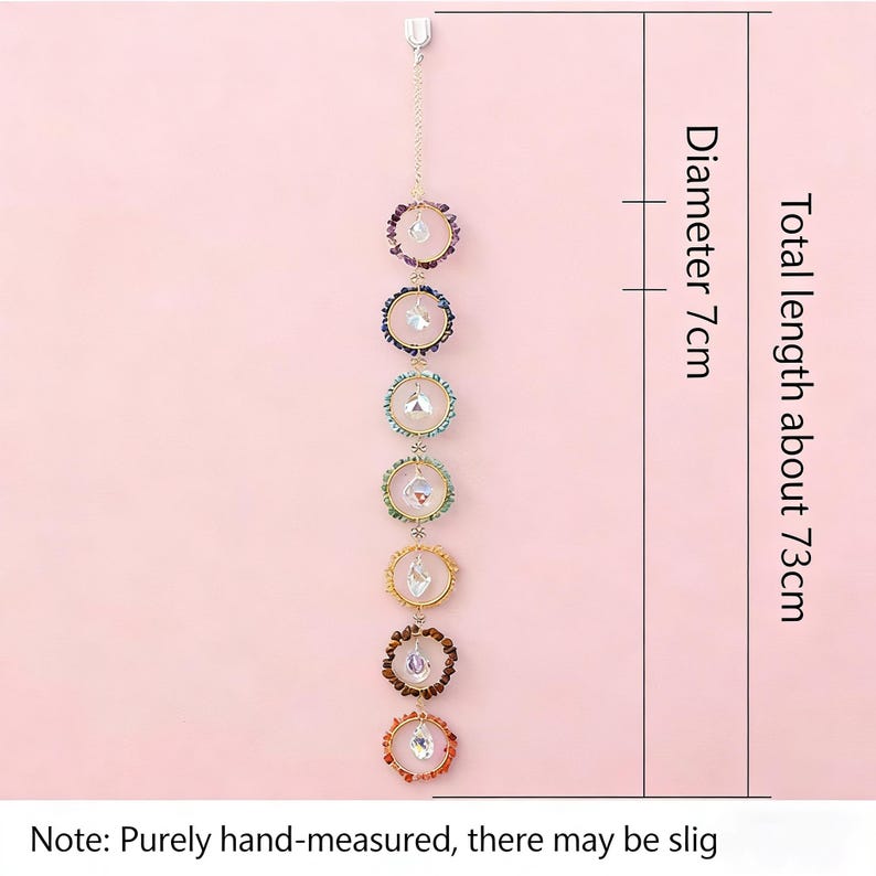 May include: A hanging chakra suncatcher featuring seven rings with gemstones and crystals. Total length is about 73cm, diameter 7cm. The rings are in various colours. The suncatcher hangs from a chain.