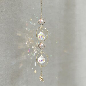 May include: A decorative suncatcher with a gold chain, featuring three clear crystal spheres, two star-shaped accents, and a crescent moon charm. The suncatcher is designed to catch and reflect light.