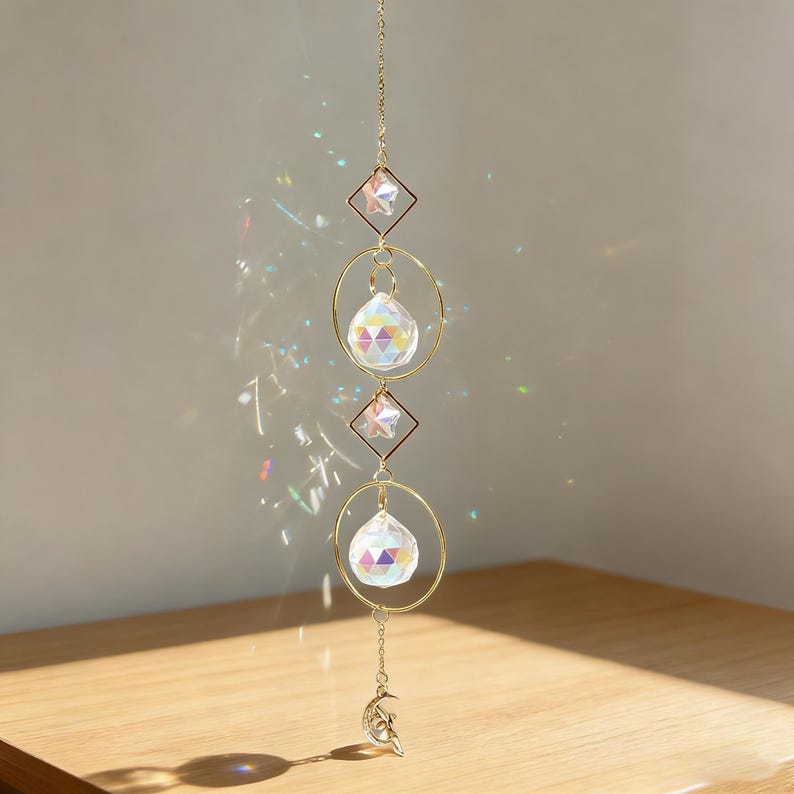 May include: A decorative suncatcher with a gold chain, geometric shapes, and crystal prisms. The suncatcher features two diamond-shaped frames with star accents, two crystal spheres, and a crescent moon charm at the bottom. The prisms cast colorful light reflections.
