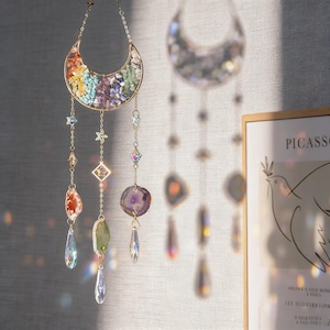 Pu&ograve; includere: Un acchiappasole decorativo a forma di mezzaluna riempita di pietre preziose colorate. L'acchiappasole &egrave; appeso a una catena dorata e presenta accenti di cristallo pendenti in varie forme e colori, tra cui stelle e gocce.